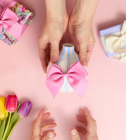 Gift box wrapped in white paper with green designs and a pink bow, held over a pink textured background.