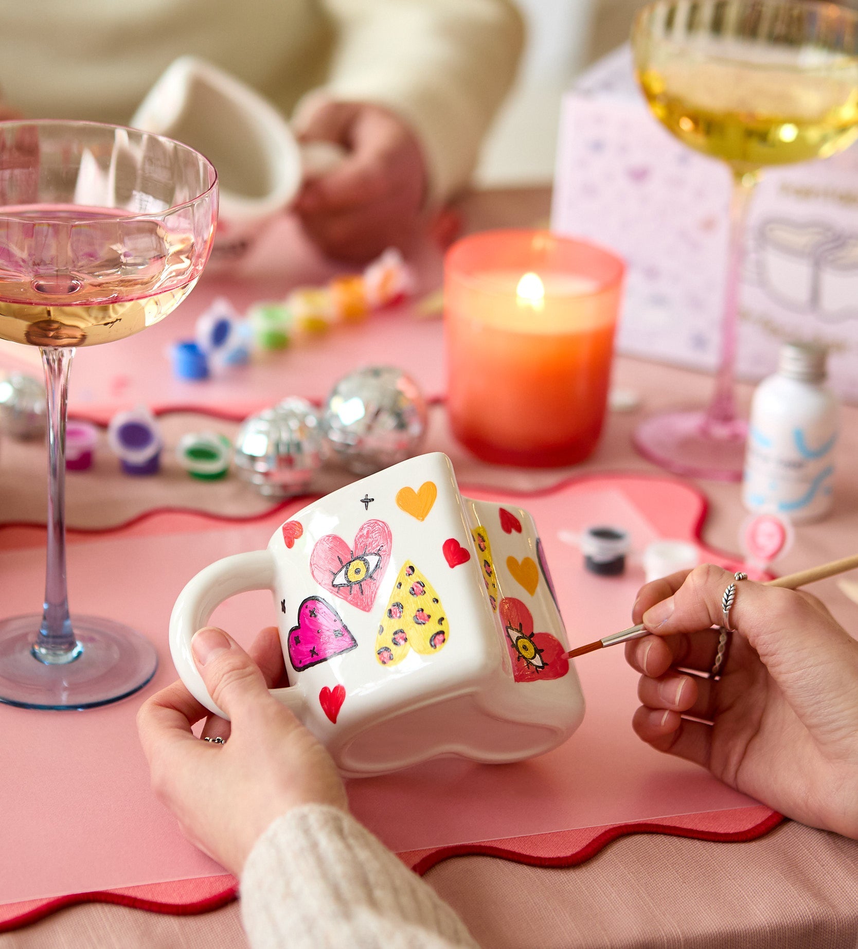 Decorative plant pot with colorful clay flowers on a marble table, surrounded by art supplies and varnish bottle.