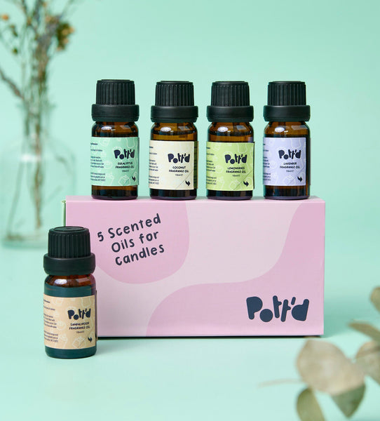 Set of five scented candle oils in amber bottles on a pastel pink and green background with minimalist design elements.