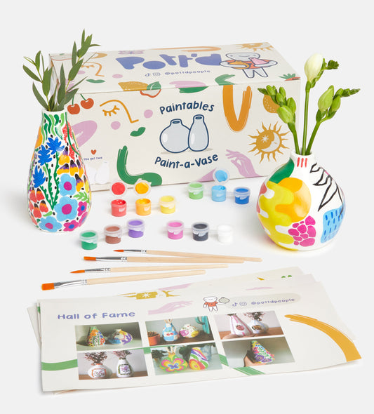 Craft kit for a gingerbread house including paint tubes, templates, varnish, and clay on a light blue background.
