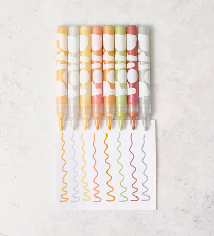 Hand painting colorful flower patterns on a mug using pastel ceramic paints with a brush, on a light gray surface.