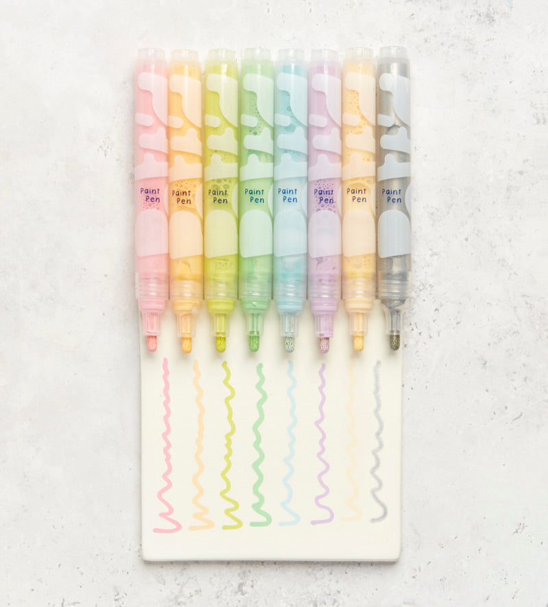 Paint-a-mug kit with a rainbow-patterned mug, colorful paints, brushes, and design inspiration booklet on a white surface.