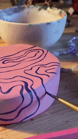 GIF of someone painting and glazing a pink and purple swirly pot