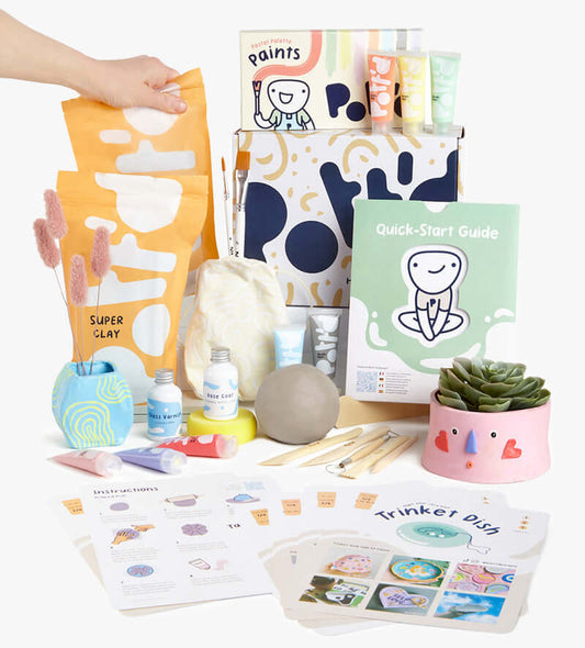 Clay skill-building kit with a colorful trinket dish, green plant pot, and speckled vase on a peach background.